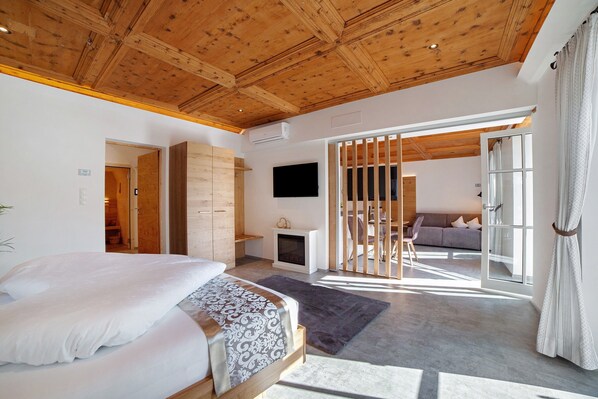 Un dormitorio con techo de madera, una cama con ropa de cama blanca, una chimenea y vistas a otra habitación por una puerta corrediza.
