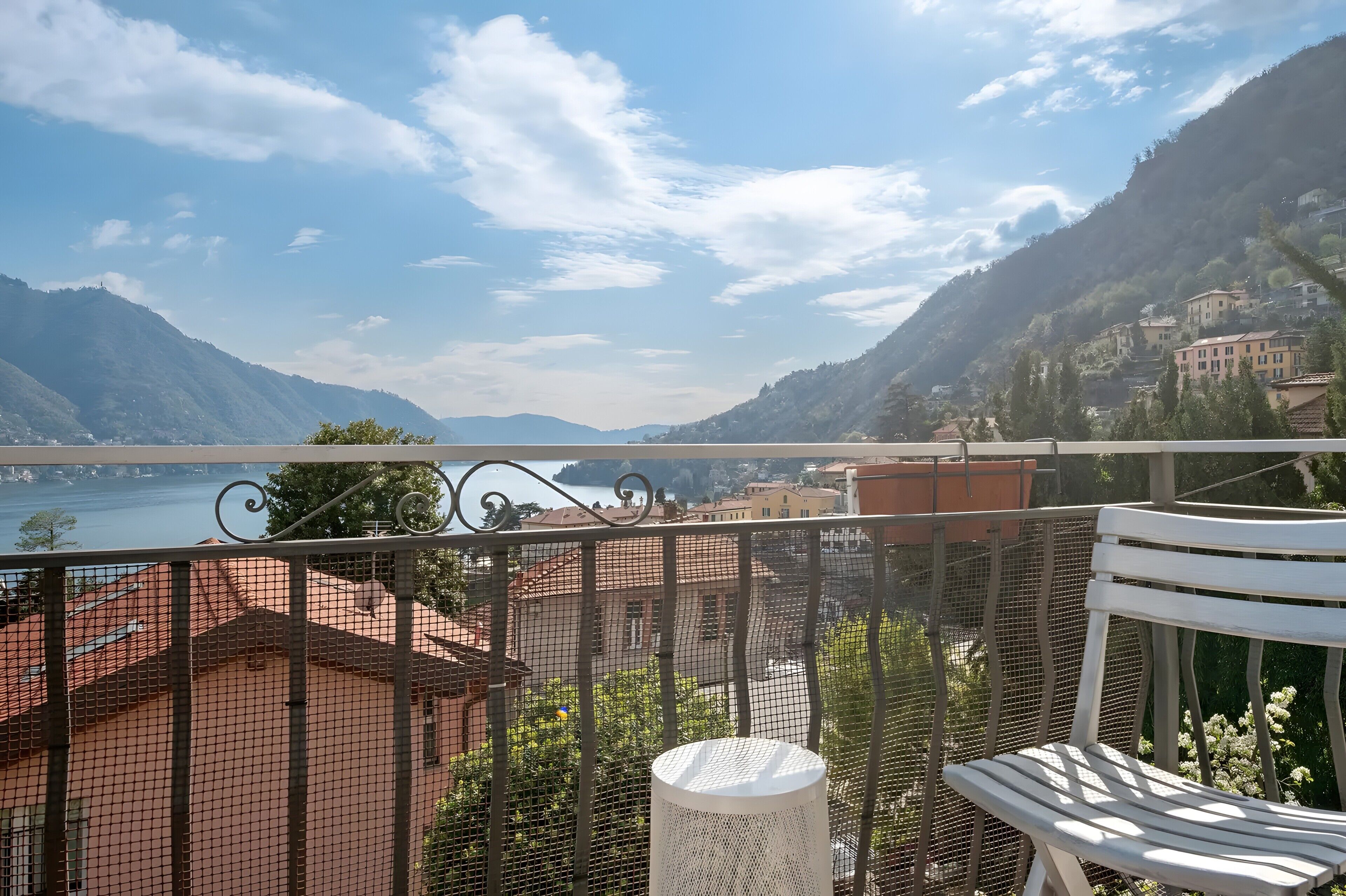 Un balcon donnant sur un lac et des montagnes, une chaise blanche et une rambarde en métal.