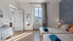 Une chambre à coucher comprenant un lit, des tables de chevet, une commode, une fenêtre donnant sur un beau paysage et un miroir.