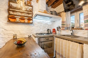 Una cocina rústica con una mesa de madera, un cuenco de fruta, una estufa a gas, un horno y una repisa con adornos.