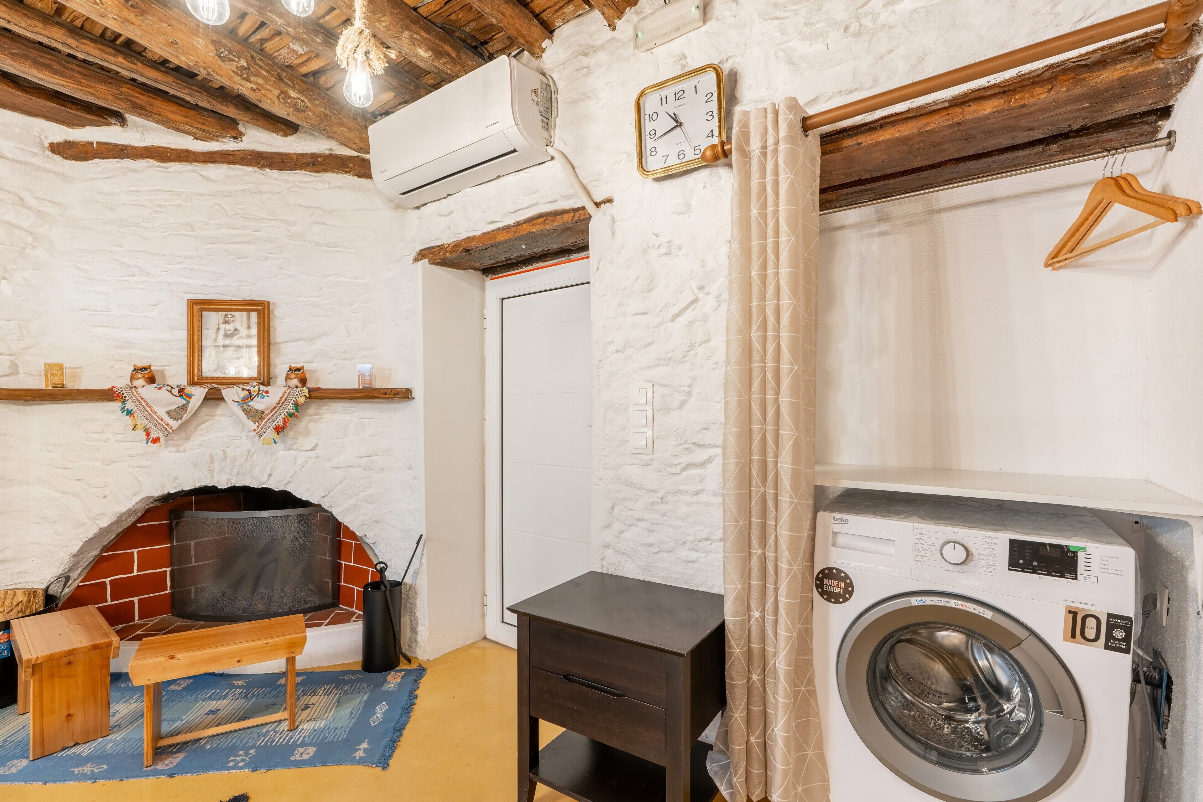 A laundry room with a washing machine, a bench, a small table, a fireplace, and a clock on the wall.