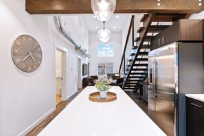 A modern kitchen with a central island, stainless steel appliances, and a wooden staircase. - New! 30-Day Rental, with communal hot tub & fitness center in Whitefish (Whitefish)