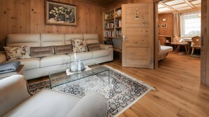 Una habitación con paneles de madera, un sofá blanco, una mesa de centro de vidrio y una estantería.