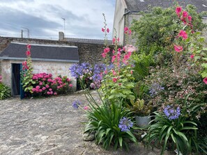 Un giardino con fiori e piante diverse, un muro in pietra e un edificio con una porta.