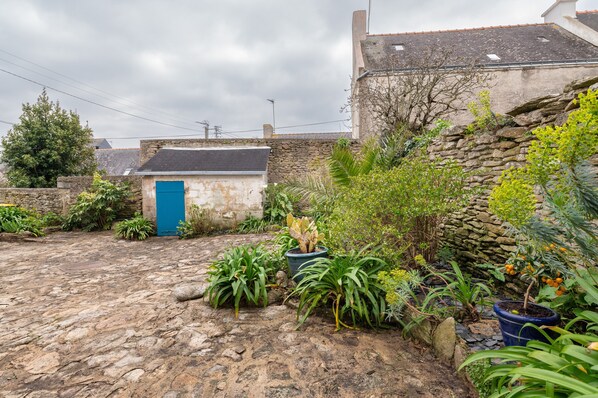 A courtyard with a stone floor, a blue door, and various potted plants.