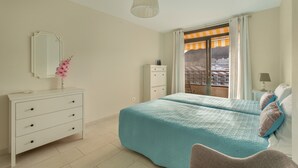 A bedroom with a bed, dresser, mirror, and a view of a building through a window. - Vacation 'Ático Home' with Sea View, Balcony and Wi-Fi (Los Cristianos)