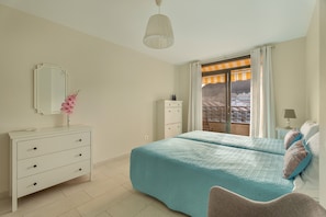 A bedroom with a bed, dresser, mirror, and a view of a building through a window. - Vacation 'Ático Home' with Sea View, Balcony and Wi-Fi (Los Cristianos)
