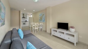 A modern living room with a grey sofa, a TV on a white stand, and a dining area in the background. - Vacation 'Ático Home' with Sea View, Balcony and Wi-Fi (Los Cristianos)