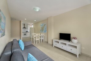 A modern living room with a grey sofa, a TV on a white stand, and a dining area in the background. - Vacation 'Ático Home' with Sea View, Balcony and Wi-Fi (Los Cristianos)