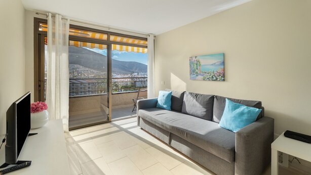 A living room with a sofa, TV, and a painting on the wall. - Vacation 'Ático Home' with Sea View, Balcony and Wi-Fi (Los Cristianos)