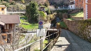 Un étroit sentier pavé de pierres menant à un pont enjambant une rivière, le tout entouré de maisons et de verdure.