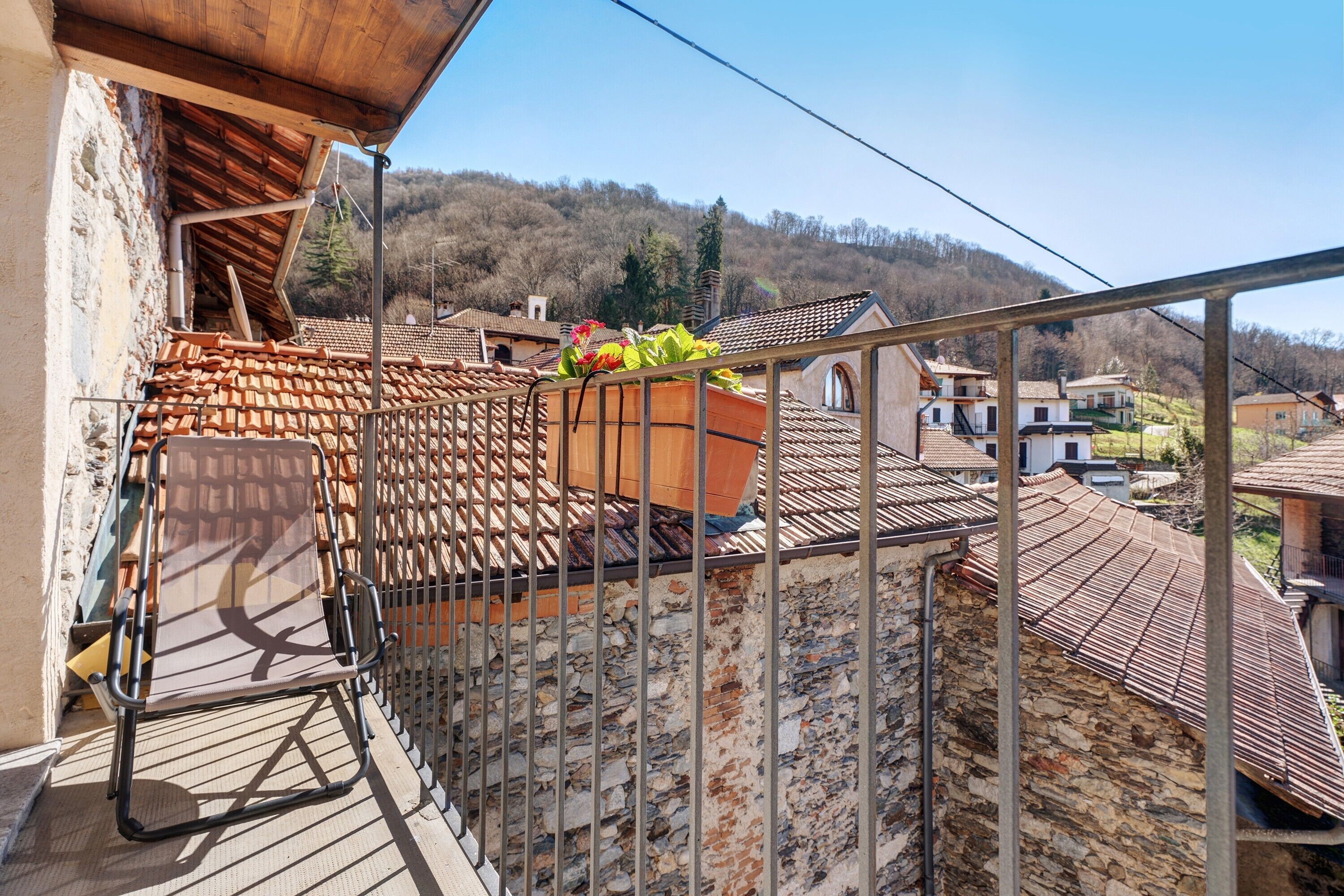Ein Balkon mit Metallgeländer, einer Steinmauer und Blick auf ein Dorf mit Terrakotta-Dächern.