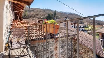 Ein Balkon mit Metallgeländer, einer Steinmauer und Blick auf ein Dorf mit Terrakotta-Dächern.