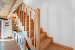 A wooden staircase leading to a second floor, a washing machine, and a kitchen area with cabinets and a sink.