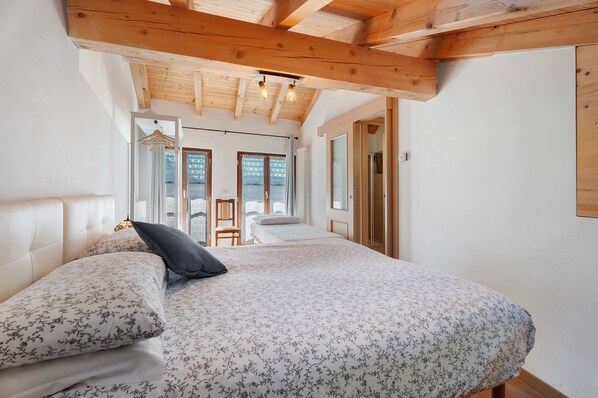 A bedroom with a bed, wooden ceiling beams, and a view of the outdoors.