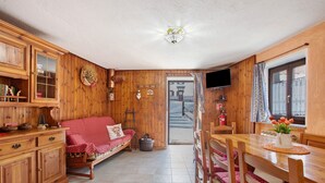 A cozy room with wooden walls, a sofa, a dining table with chairs, a television, and a window with curtains.