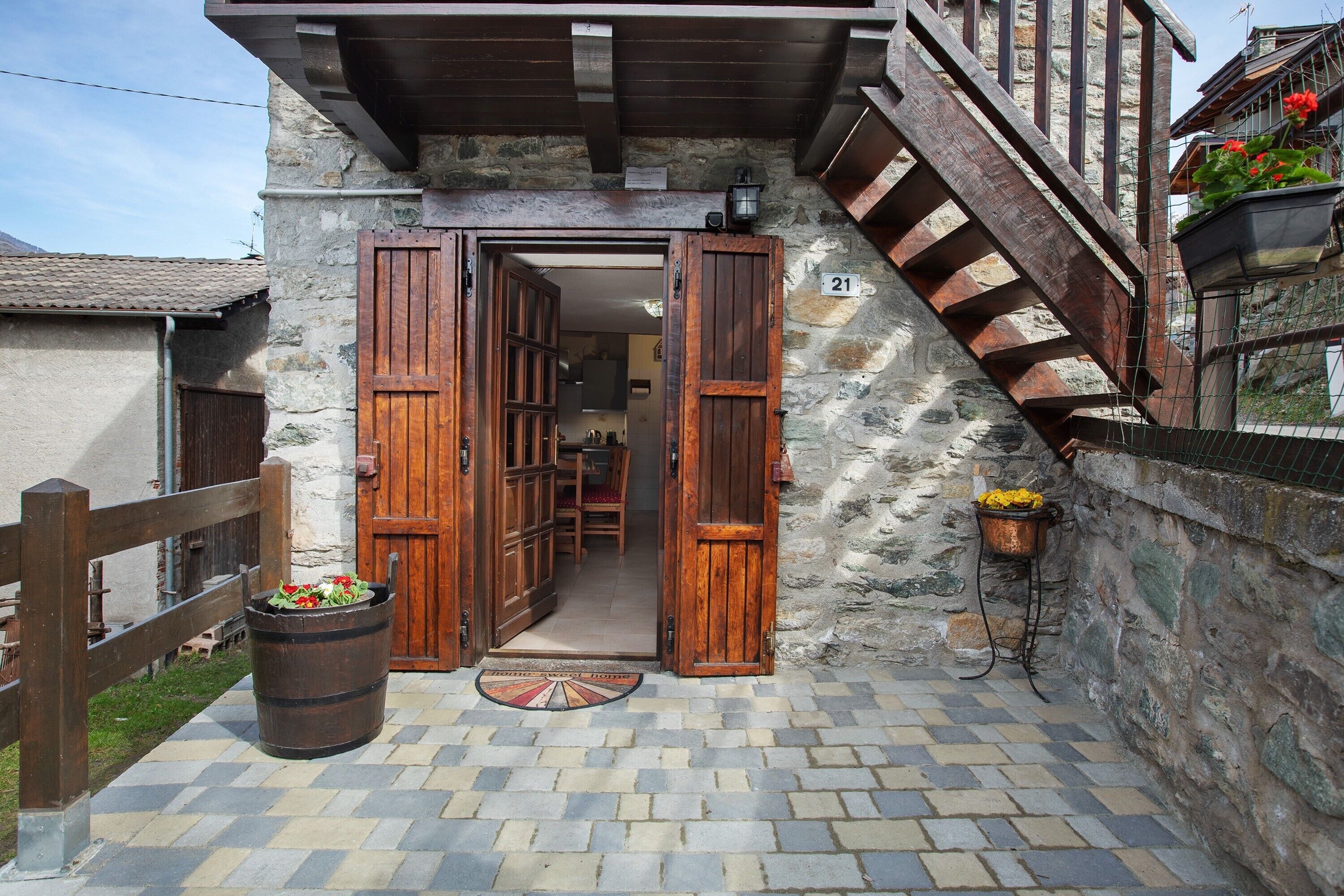 A stone building with wooden doors, a wooden staircase, and a number 21 sign.