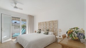 A hotel room with a bed, a glass door leading to a balcony, a dining table with chairs, and a decorative wall panel. - Vacation Villa 'Spinnaker Playa' with Sea View, Private Terrace and Wi-Fi (Santiago del Teide)