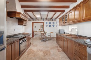 A kitchen with wooden cabinets, granite countertops, a dining area with chairs, and a tiled backsplash.