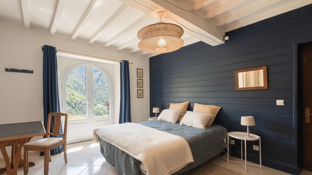 Un dormitorio con cama, escritorio, silla, ventana con cortinas, ventilador de techo y una lámpara de pared.