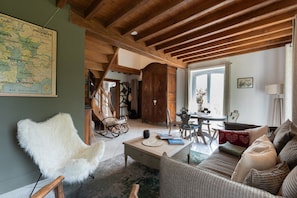 Uma sala de estar aconchegante com um mapa, vigas de madeira, uma cadeira branca, um sofá e um espaço de jantar.