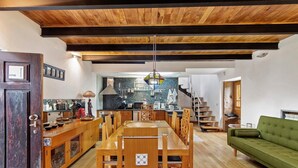 A spacious living area with a wooden dining table, a green sofa, and a kitchen in the background. - Holiday Home 'Quinta Das Cavadas' with Mountain View, Private Pool and Wi-Fi (Canedo)