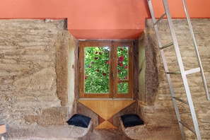 Ein Zimmer mit einer Steinwand, einem Holzfenster mit Glasscheiben und einer Leiter.