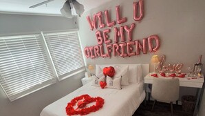 Een slaapkamer met een bed, een plafondventilator, een nachtkastje en een wanddecoratie.