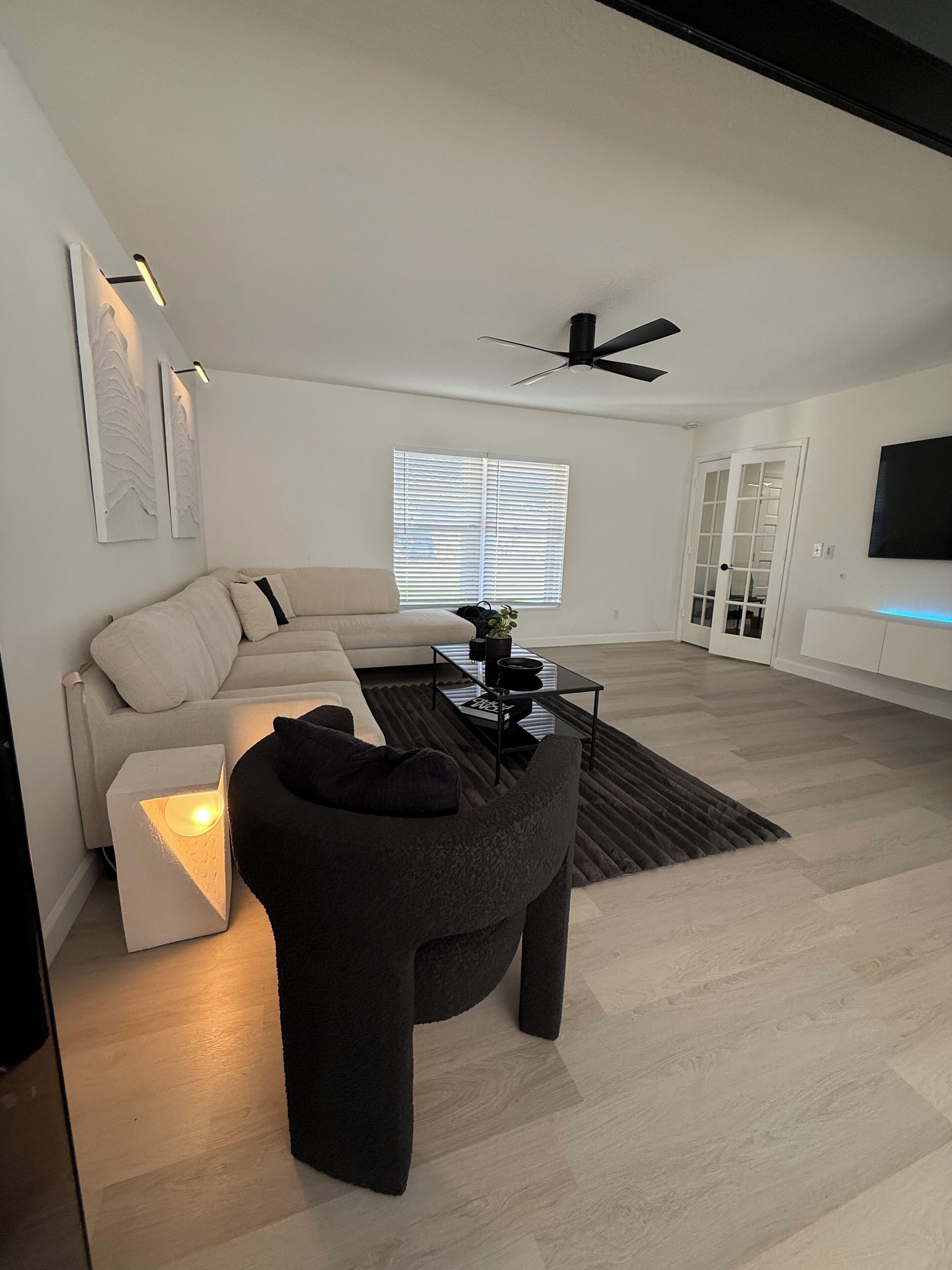 A modern living room with a sectional sofa, a dark armchair, a coffee table, and a ceiling fan.