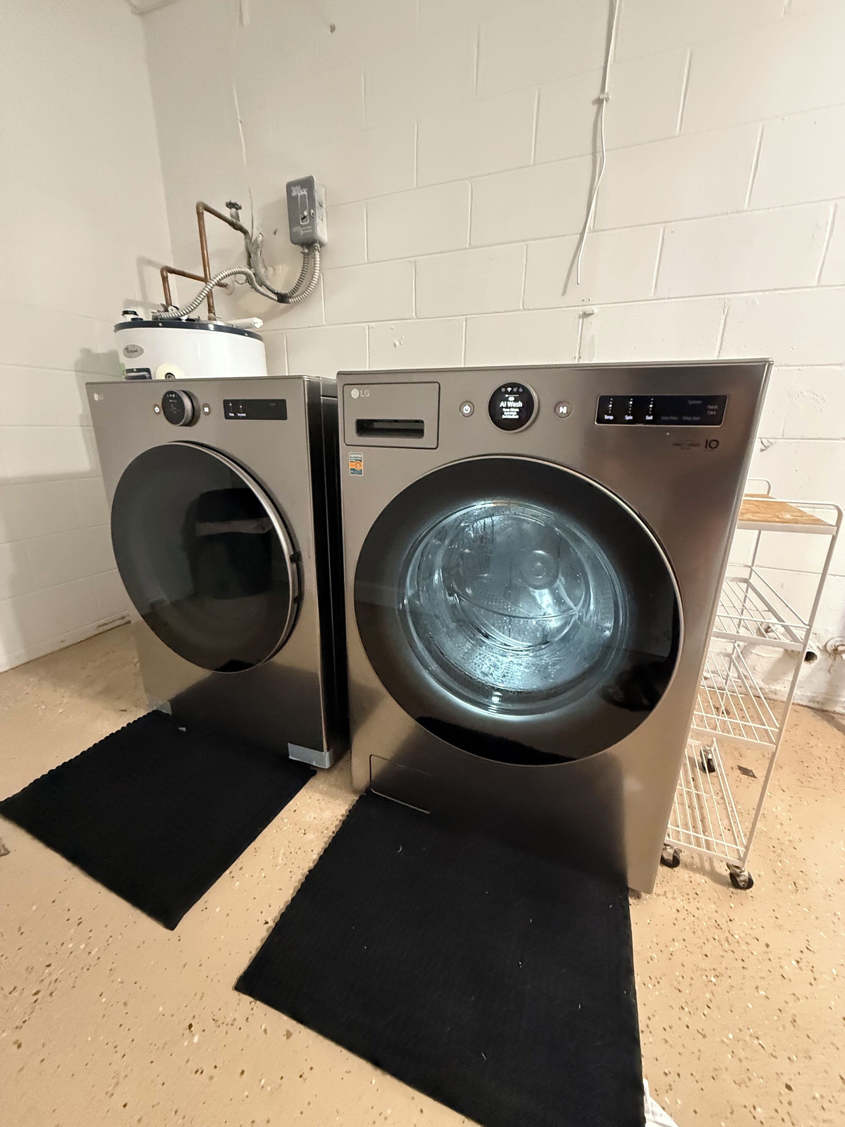 Two front-loading LG washing machines in a laundry room with a white tiled wall and a metal rack.