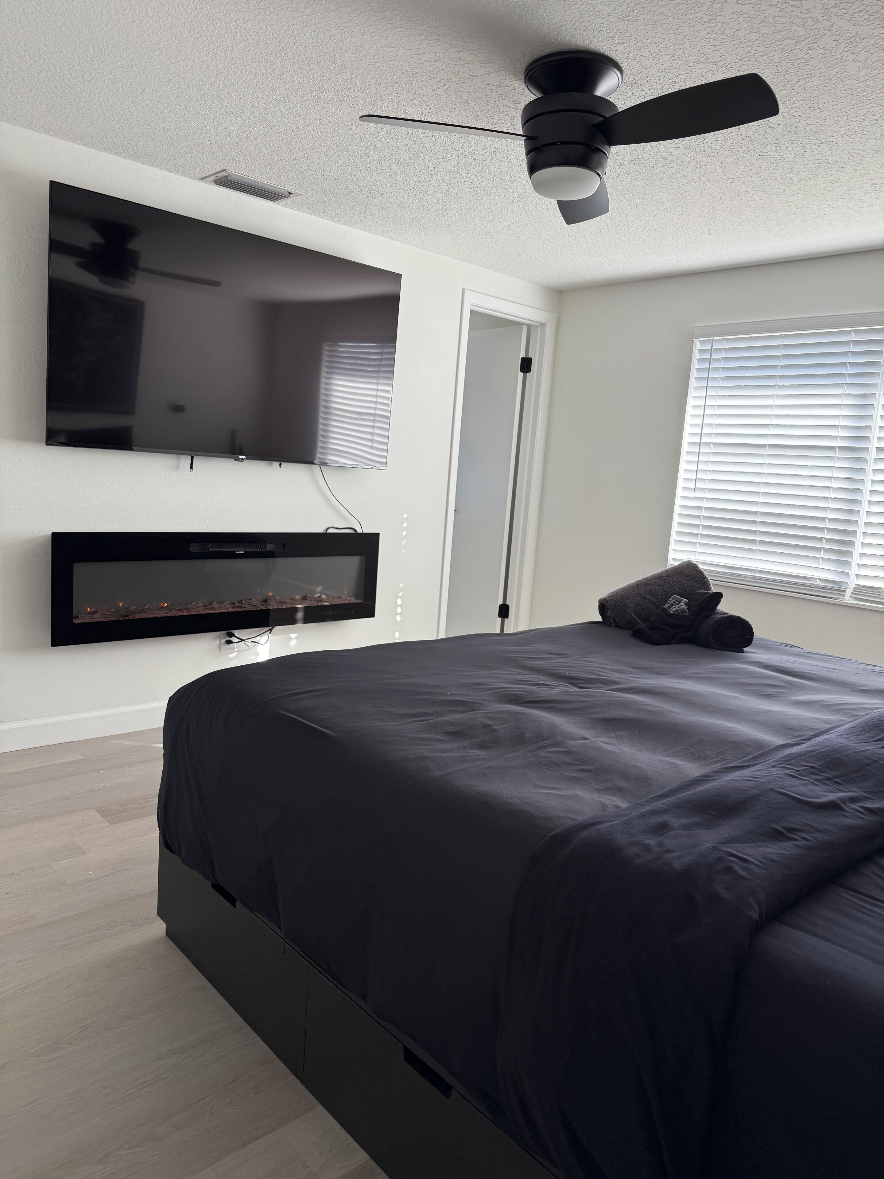 A modern bedroom with a large bed, a mounted TV, and a ceiling fan.