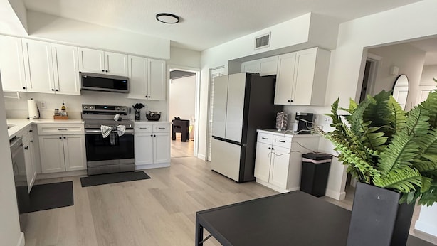 A modern kitchen with white cabinets, stainless steel appliances, and a black countertop. - ‘The Gallery’ Spacious & Modern 4 Bedroom Getaway with Pool (Tampa)