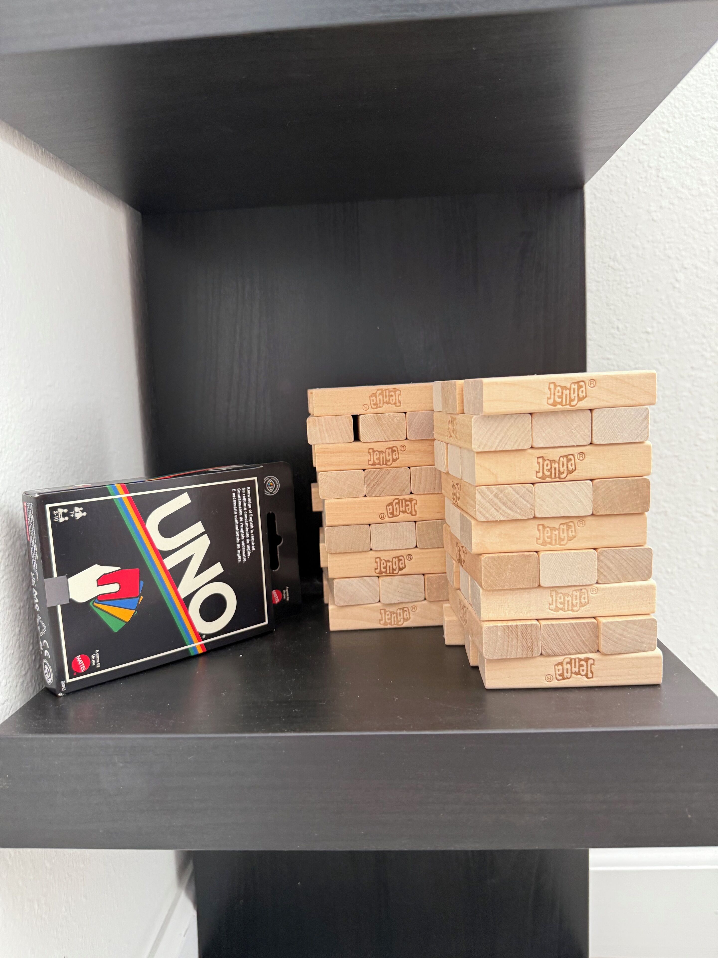 A black shelf with a UNO game box and wooden Jenga blocks.