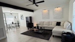 A modern living room with a sofa, coffee table, and a dining area with chairs and a table. - ‘The Gallery’ Spacious & Modern 4 Bedroom Getaway with Pool (Tampa)