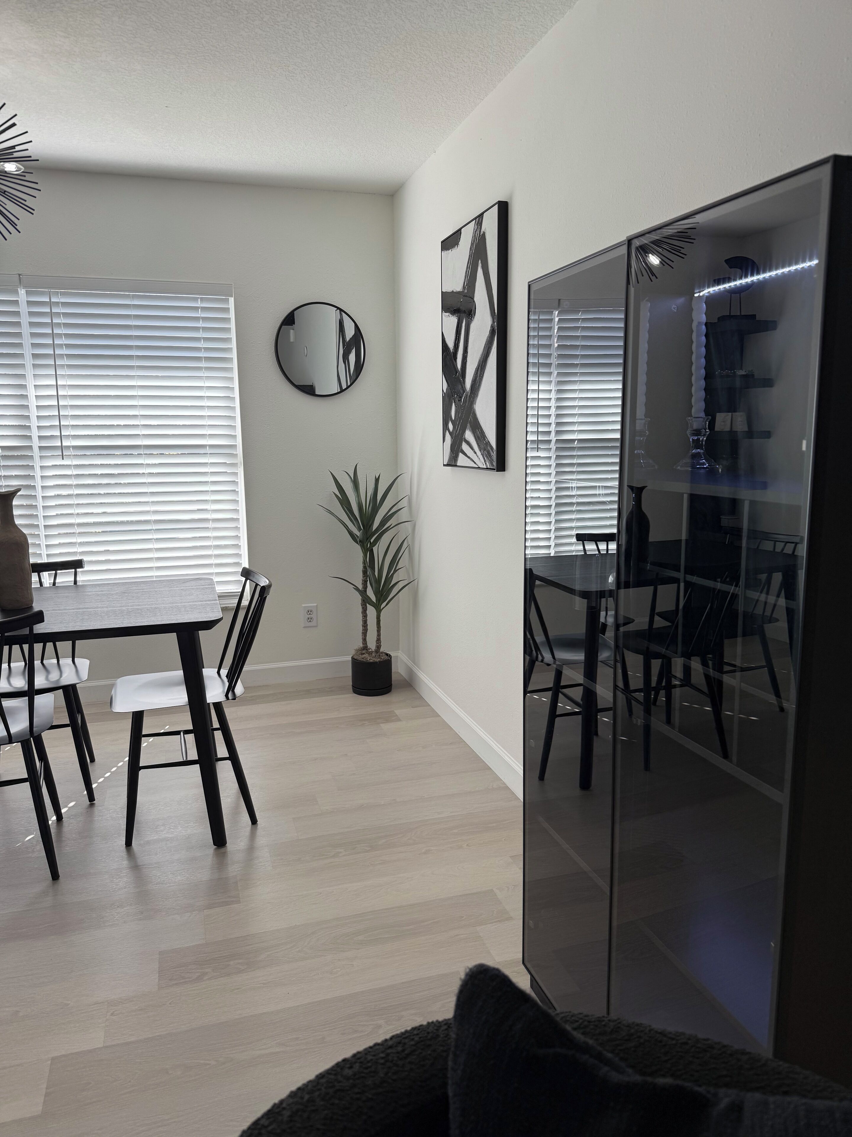 Een moderne eetruimte met een ronde tafel, stoelen, een potplant en een grote spiegel aan de muur.