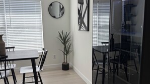A modern dining area with a round table, chairs, a potted plant, and a large mirror on the wall. - ‘The Gallery’ Spacious & Modern 4 Bedroom Getaway with Pool (Tampa)