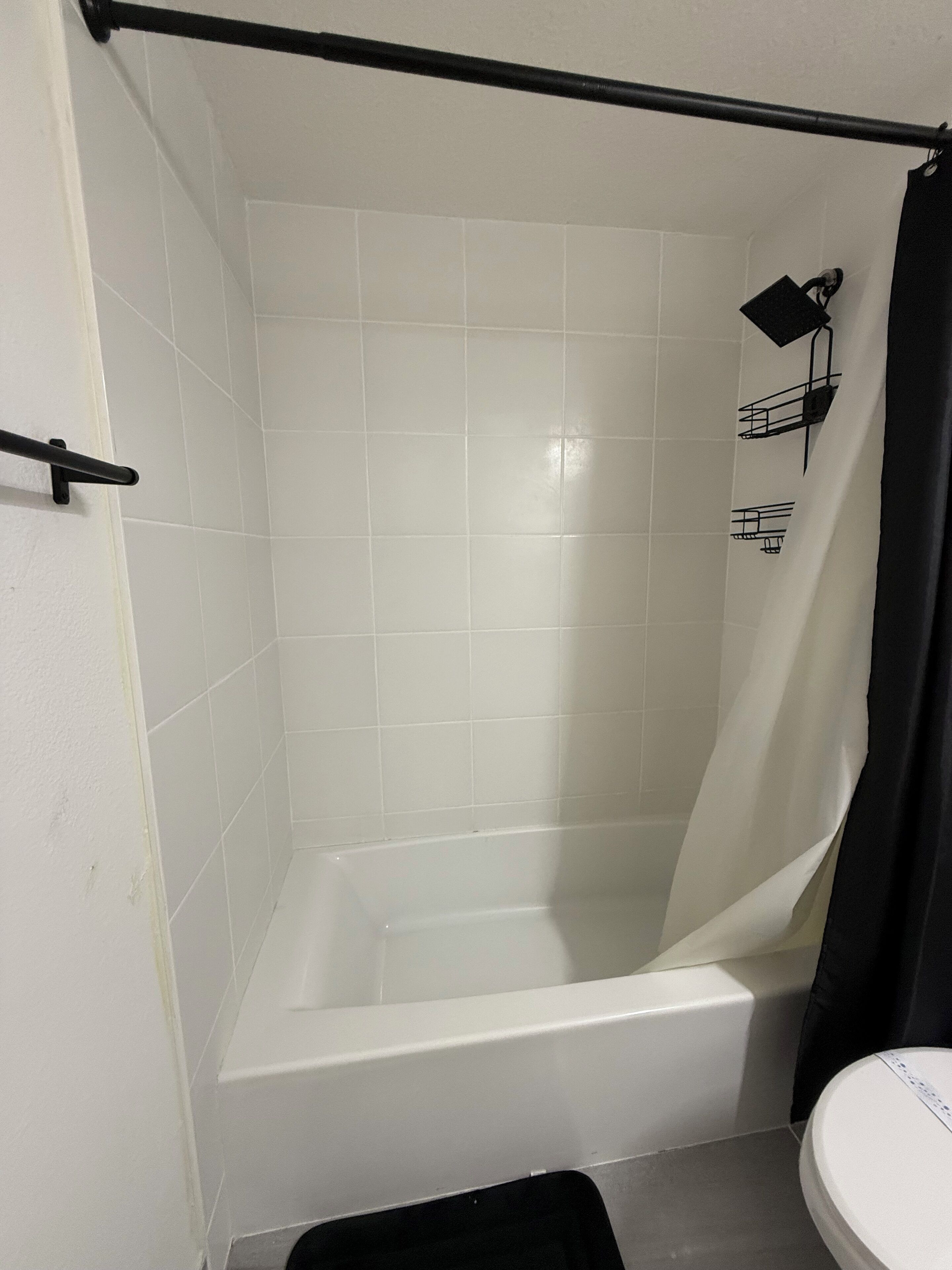 A bathroom with a white bathtub, a black shower curtain, and a white toilet.
