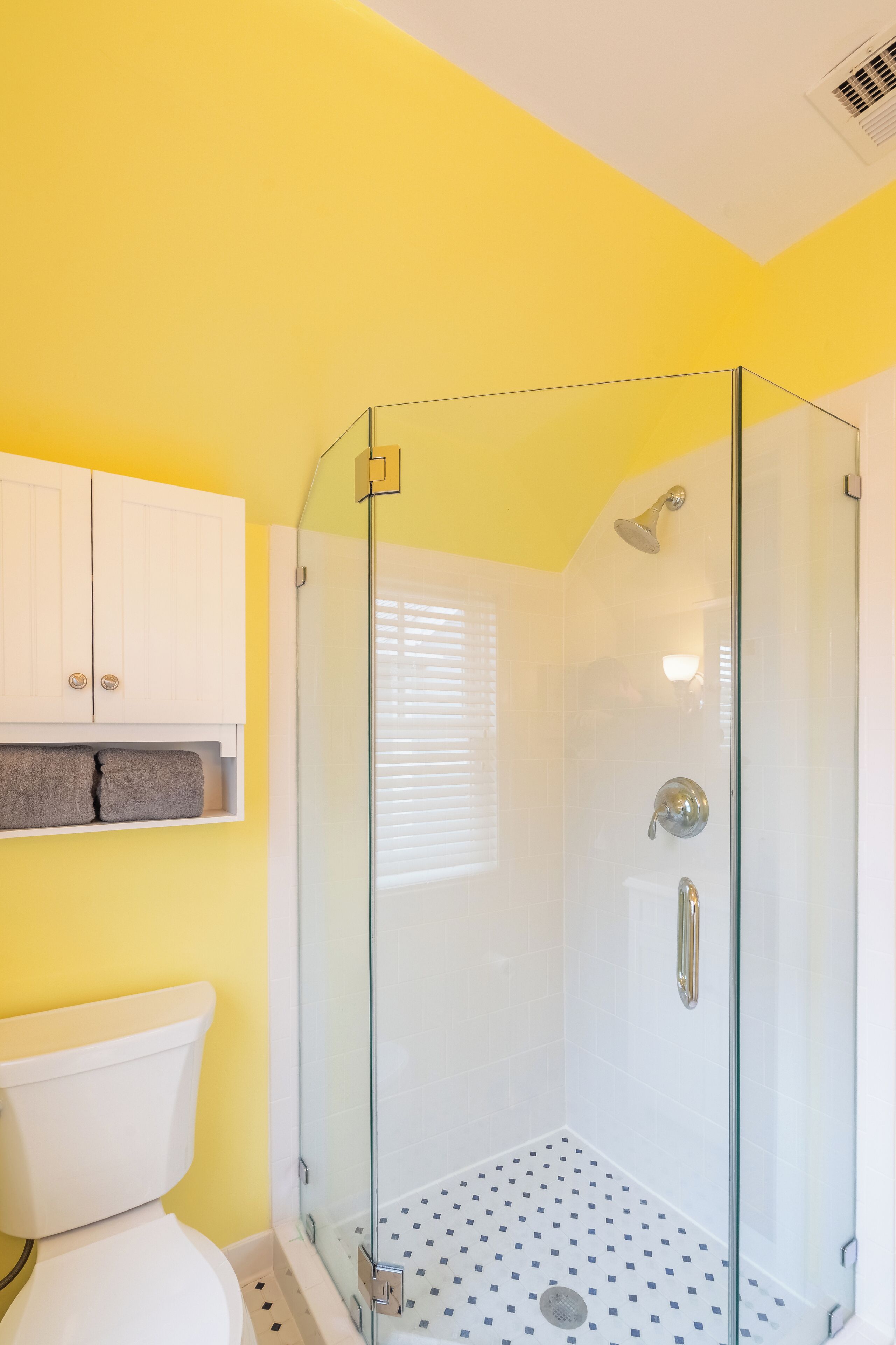 Une salle de bain avec une douche à parois de verre, des toilettes blanches et un mur jaune.