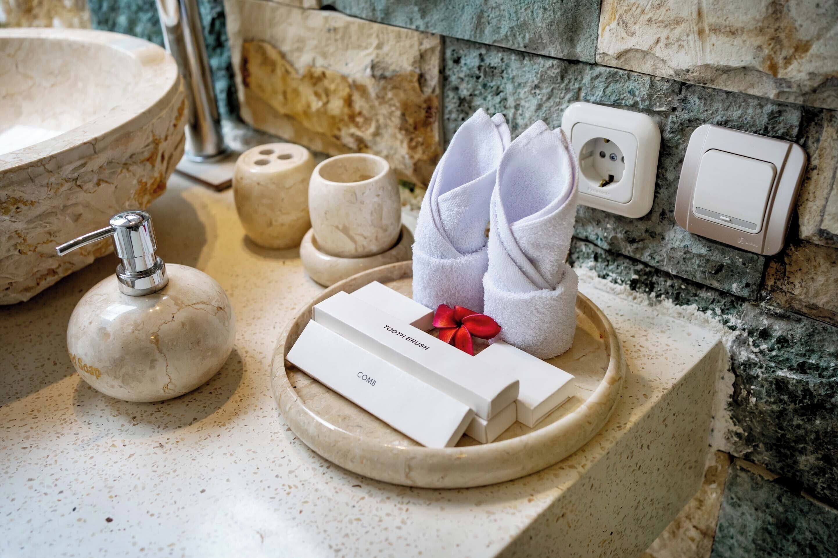 Un mobile bagno con lavabo in marmo, un dispenser per sapone, un porta spazzolini e un portaserviti con asciugamani.