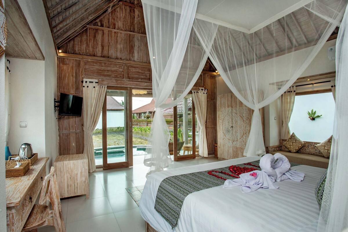 A bedroom with a large bed, a television, and a view of the outdoors.