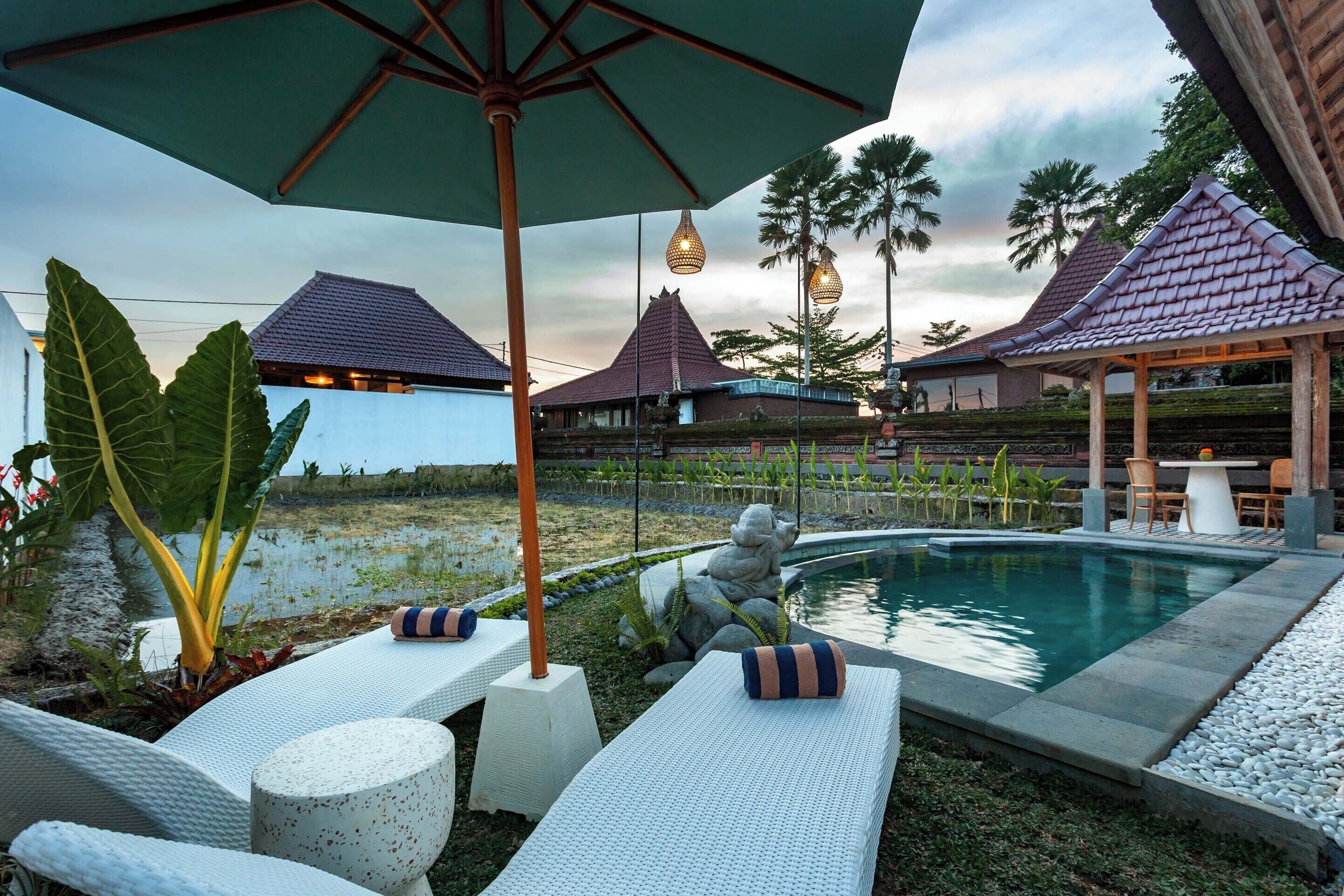 A pool area with lounge chairs, umbrellas, and a stone statue.