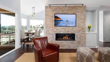 A modern living room with a stone fireplace, a leather armchair, and a television mounted on a stone wall.