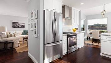 A modern kitchen with stainless steel appliances, a dining area with a view, and a living room with a sofa and coffee table.