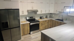 A modern kitchen with white cabinets, a stainless steel refrigerator, a black stove, and a wooden countertop.