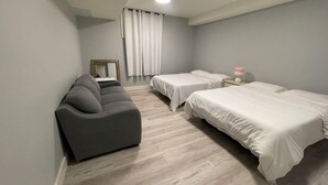A room with two beds, a gray sofa, a mirror, and a ceiling light.