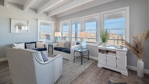 A spacious living room with a large window, a white cabinet, and a comfortable seating area. - Pinstripe Paradise-Kitty Hawk MP 5, Ocean View, 10 Yds to Beach, Pool, Hot Tub, Pets OK, Flex Stays (Kitty Hawk)