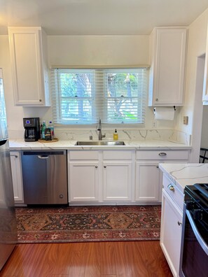A kitchen with white cabinets, a stainless steel dishwasher, a double sink, and a patterned rug.