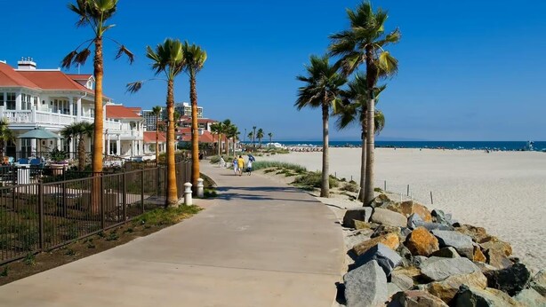 A beachfront walkway lined with palm trees and a building with a red roof. - Charming, Historic 2-bedroom house in Coronado…28+ day discount (Coronado)