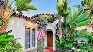 A house with a red pathway leading to a wooden door, surrounded by lush greenery and an American flag. - Charming, Historic 2-bedroom house in Coronado…28+ day discount (Coronado)