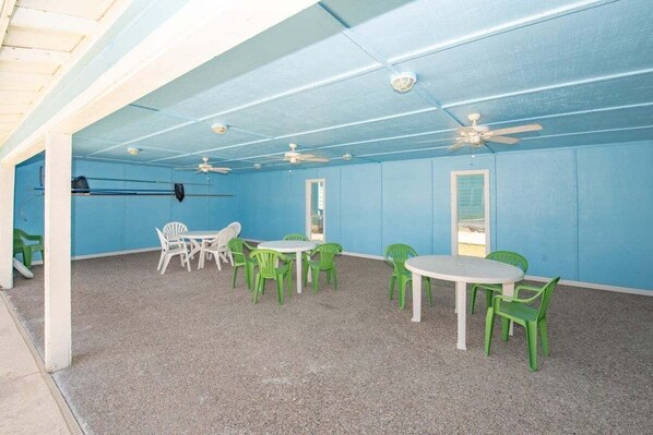 A room with blue walls, white ceiling, and a ceiling fan. There are green and white chairs around a white table.